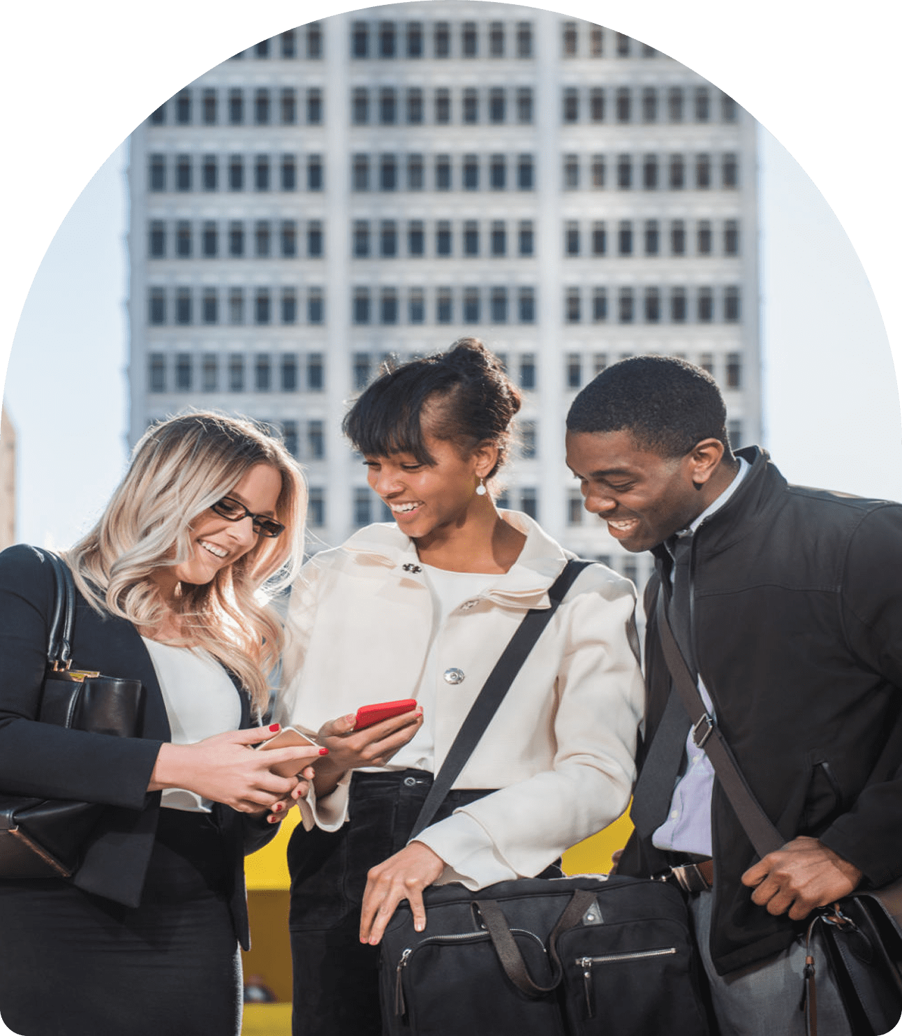 Three people smiling at phone outside building.